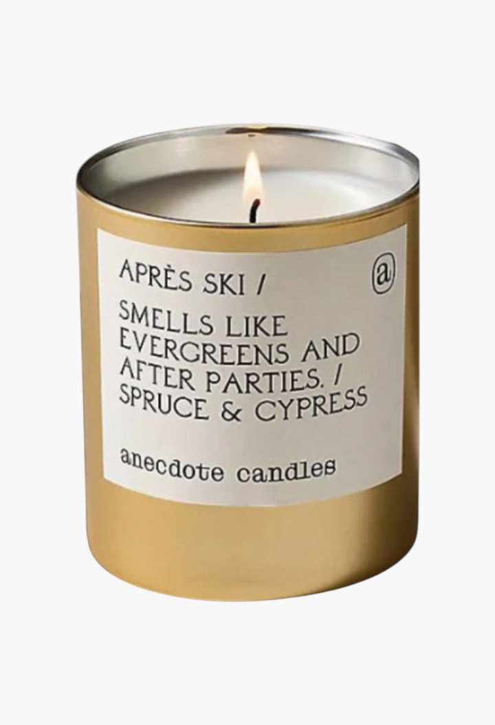 GLAM MODA Anecdote Gourmand candles in gold glass vessels with printed labels featuring cozy winter scent descriptions.