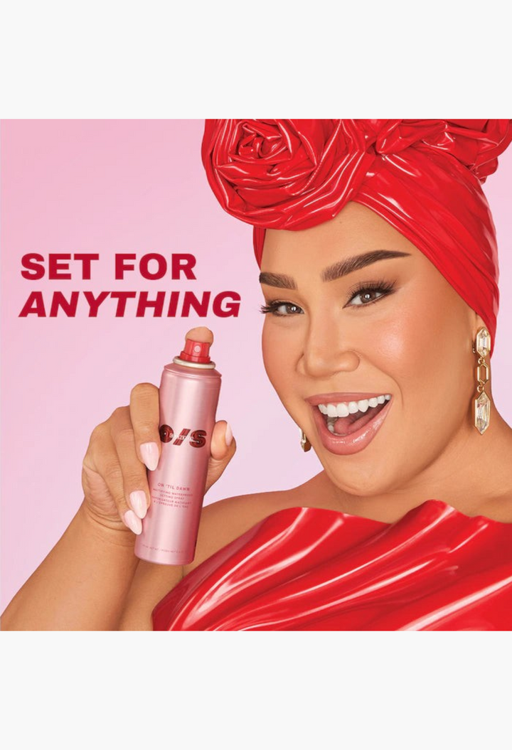 GLAM MODA On 'Til Dawn mattifying waterproof setting spray held by a smiling model wearing a red headwrap and top.